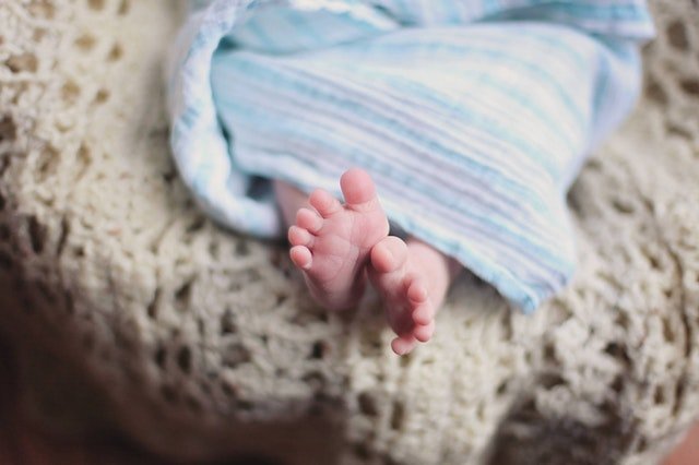 Nohy bábätka ležiaceho na posteli a zabaleného v modrej deke
